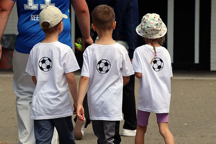 Drei Kinder in weißen Trikots von hinten mit je einem Fußball auf dem Trikot