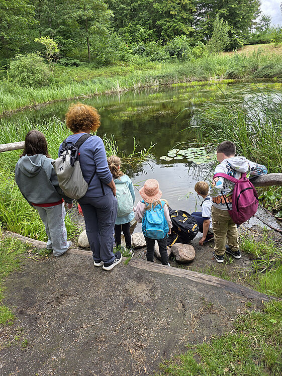 Kindergruppe und eine Erwachsene in der Natur am Rand eines Teichs