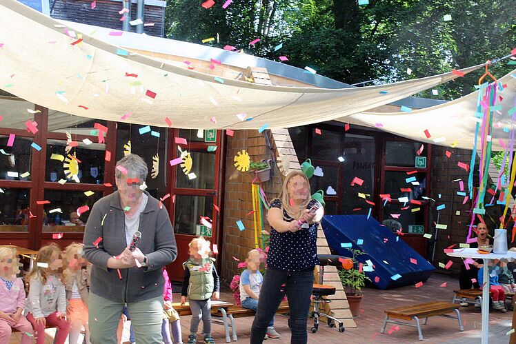 Erwachsene mit Konfetti-Kanonen, Kinder schauen zu.