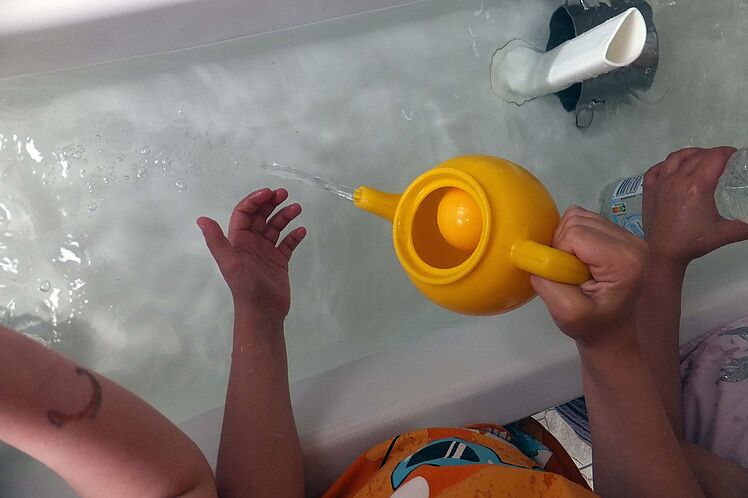 Kinderhände mit gelber Gießkanne, gießen Wasser in volle Badewanne
