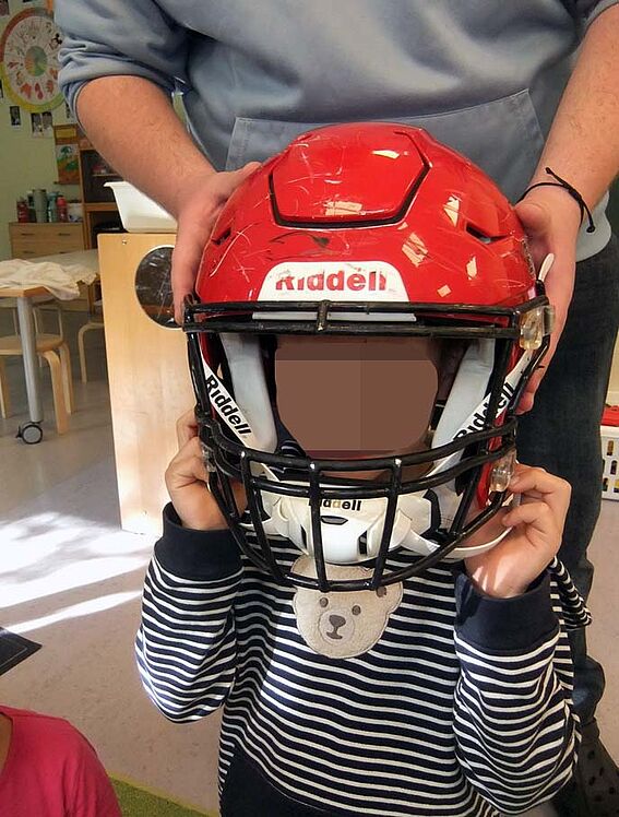 Kind mit Football-Helm, hinter ihm steht ein Erwachsener