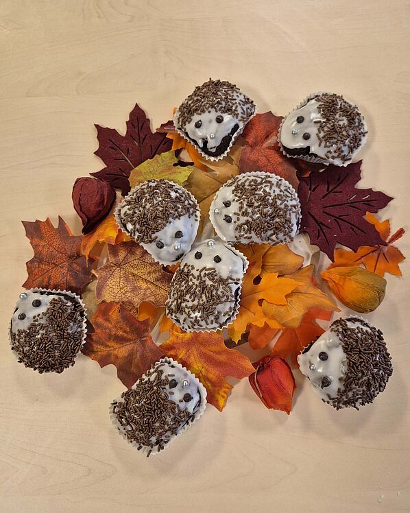 Igel-Muffins mit Schokostreuseln und Schokoaugen auf einer Laub-Deko