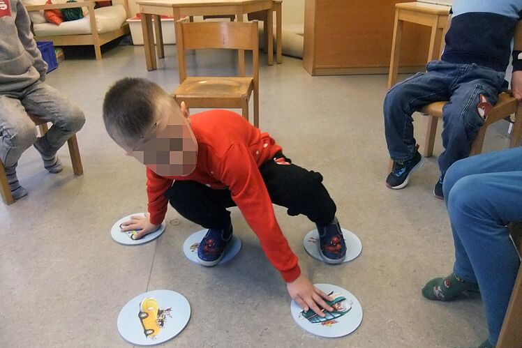 Kind versucht, mit Armen und Beinen verschiedene Symbolkärtchen auf dem Boden zu erreichen