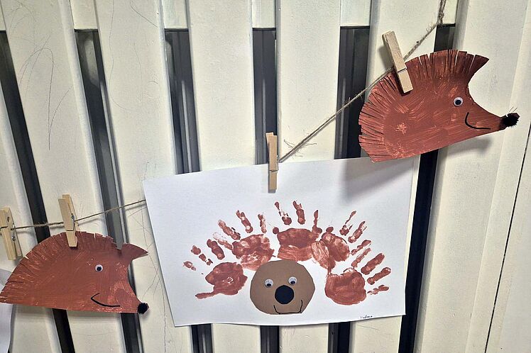 Mit Klammern an einer Leine aufgehängte Igel aus Papier und ein Bild mit einem Igel aus Handabdrücken