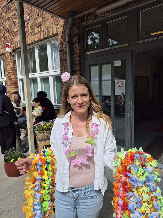 stellvertretende Kitaleiterin mit bunten Blumenketten auf beiden Armen vor dem Kita-Gebäude