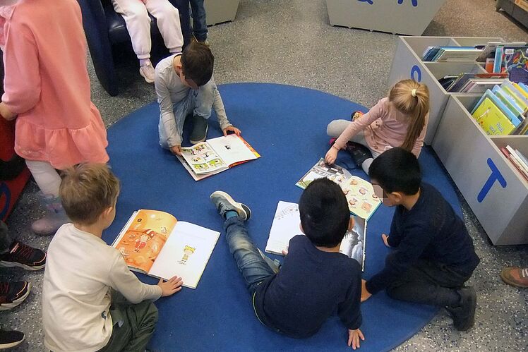 Kinder sitzen auf dem Boden und schauen Bücher an