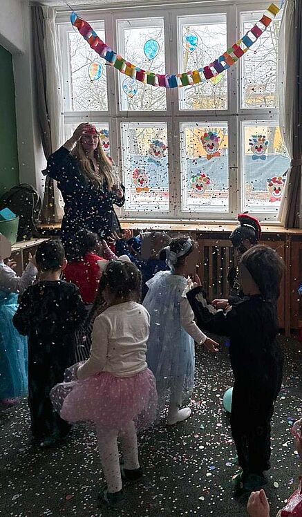 Erzieherin und verkleidete Kinder im Konfettiregen