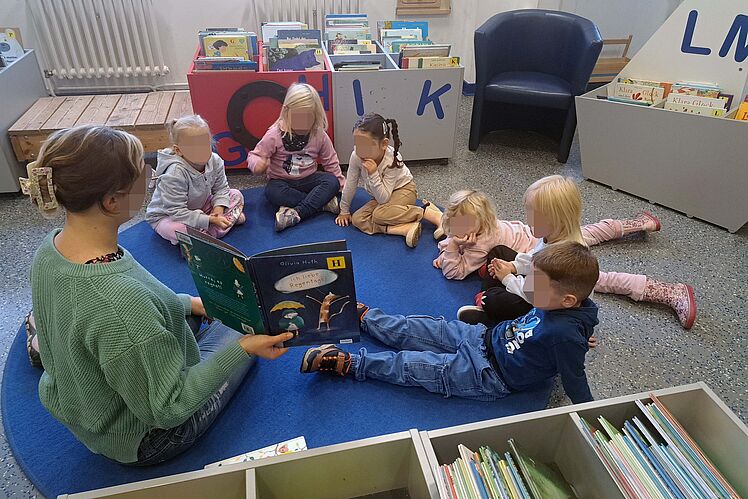 Sechs Kinder sitzen im Kreis auf dem Boden und bekommen das Buch "Ich liebe Regentage" vorgelesen.