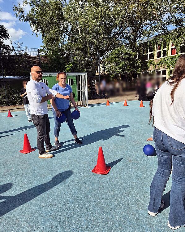 Erwachsene und Kinder auf dem Sportplatz mit aufgestellten Kegeln und Bällen