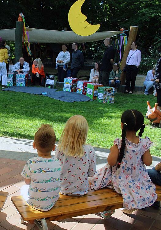 Kinder und Erwachsene im Kita-Außenbereich, zu sehen ist die Deko der "Mond"-Gruppe.