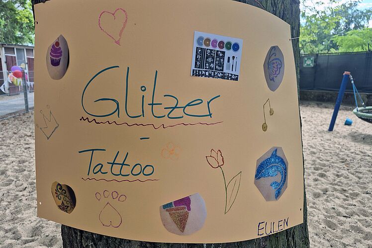 An einem Baumstamm befestigtes Plakat zur Aktion "Glitzertattoos"