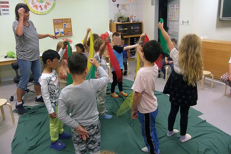 Kinder und Erzieherin tanzen mit bunten Bändern in den Händen