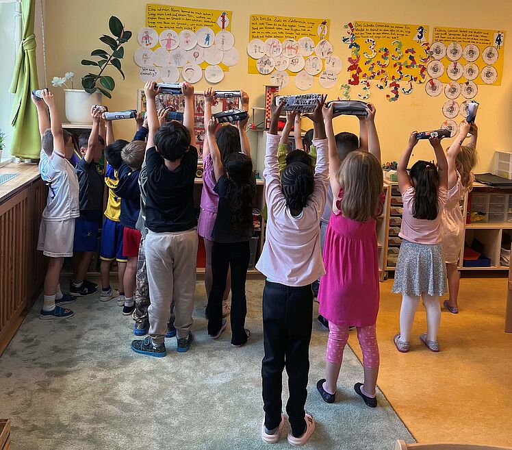 Kinder der Kita Sternschnuppe halten ihre Federmäppchen in die Luft (von hinten fotografiert)