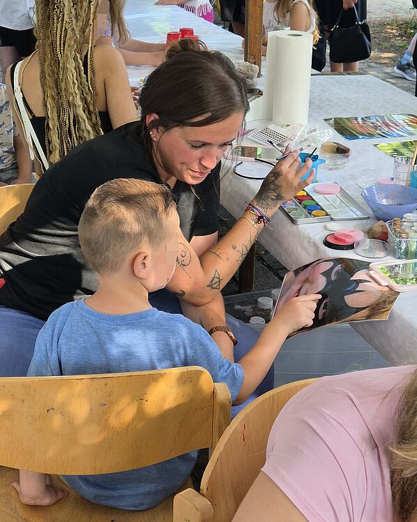 Frau mit Kind, dass sich ein Superhelden-Motiv fürs Face Painting aussucht.