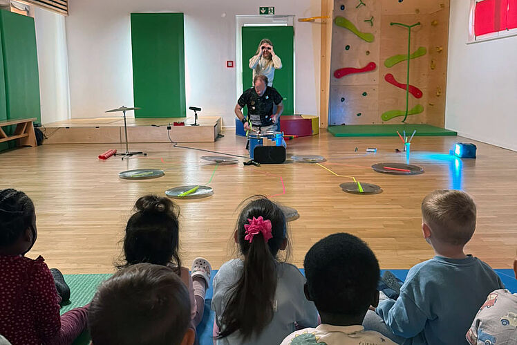 Kinder (von hinten) schauen im Turnraum der Kita einer Theateraufführung zu