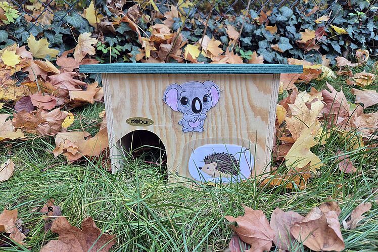 Selbst gebautes Igel-Häuschen vor einem Laubhaufen auf der Wiese