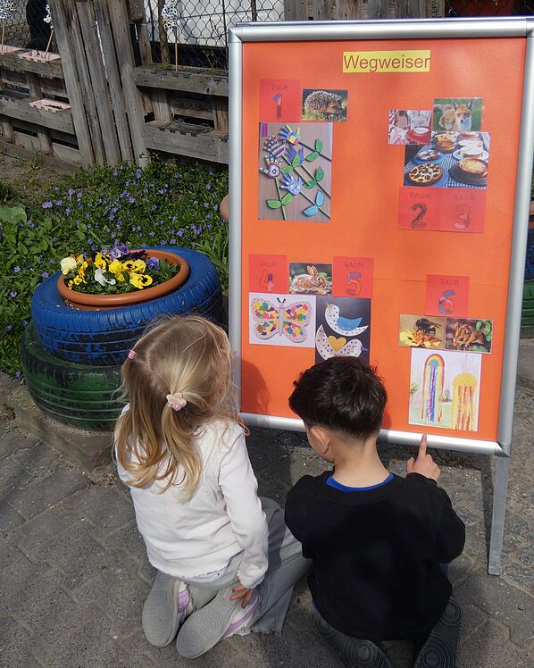 Zwei Kinder knien am Eingang vor dem Wegweiser der Frühlingswerkstatt mit den Musterbildern.