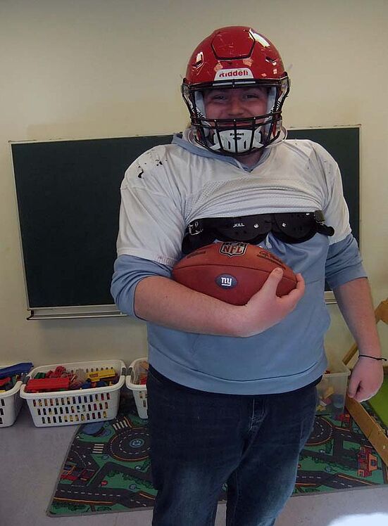 Erzieher mit Football-Helm und Football im Arm