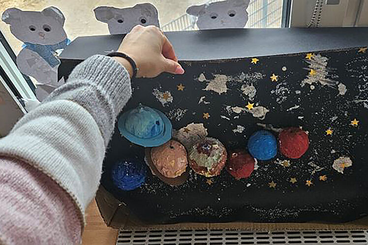Kinderhand zeigt auf selbst gebasteltes Planetensystem
