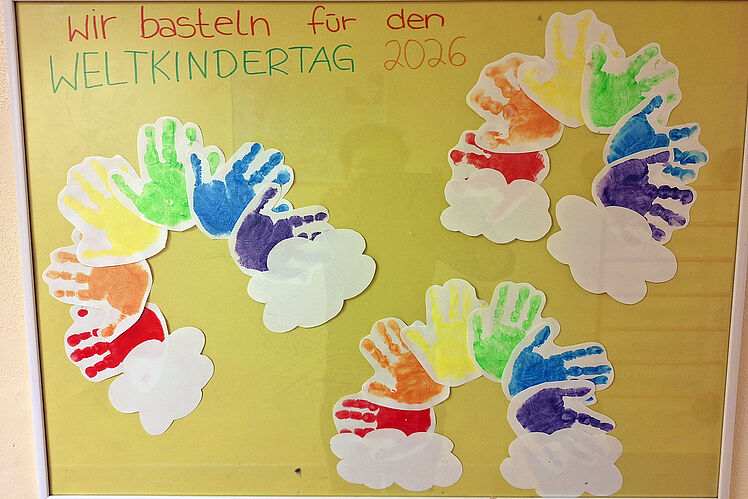 Aushang "Wir basteln für den Weltkindertag" mit Handabdrücken in Regenbogenfarben und -form