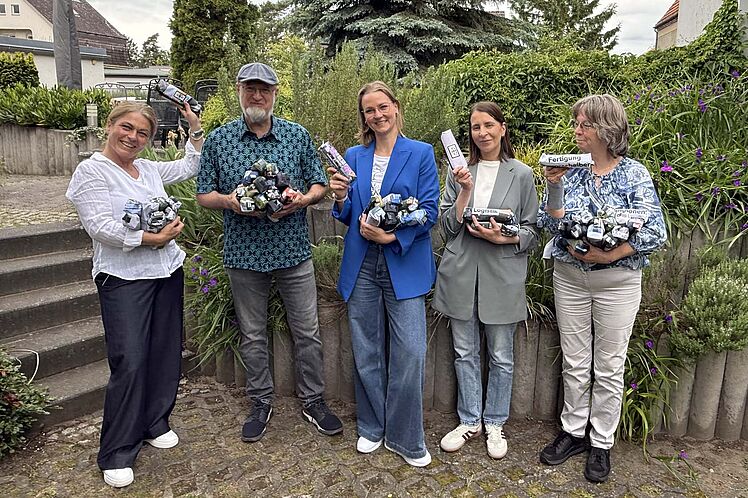 Gruppenfoto: Vertretungen AWO Spandau und BMW Motorradwerk, alle mit einigen Federmäppchen in den Händen (im Garten fotografiert)