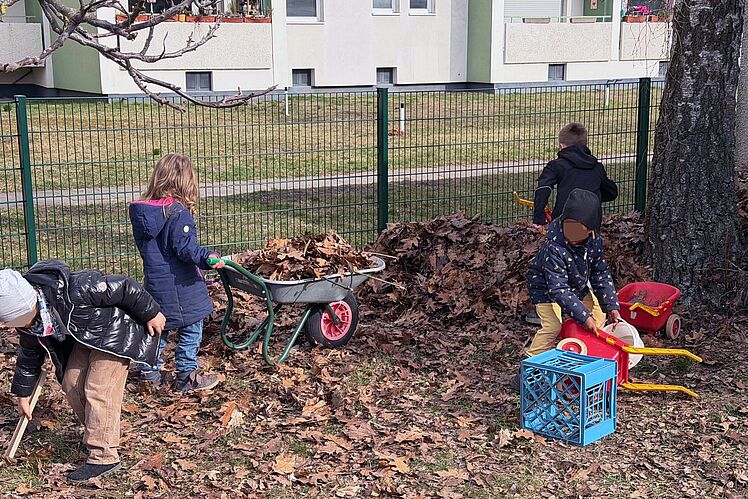 Kinder mit großen und kleinen Schubkarren räumen Laub beiseite.