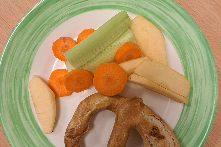 Ausschnitt eines Tellers mit Brezel und Rohkost