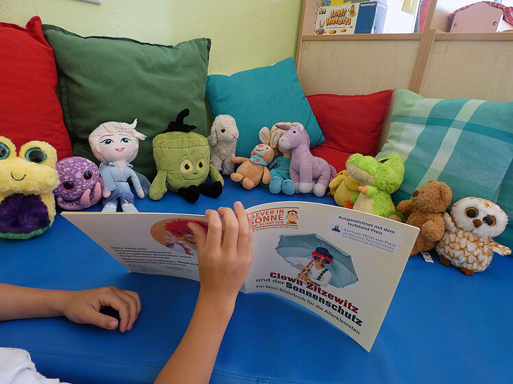 Kinderhände halten Infoheft vor "Publikum" aus Plüschtieren auf dem Sofa