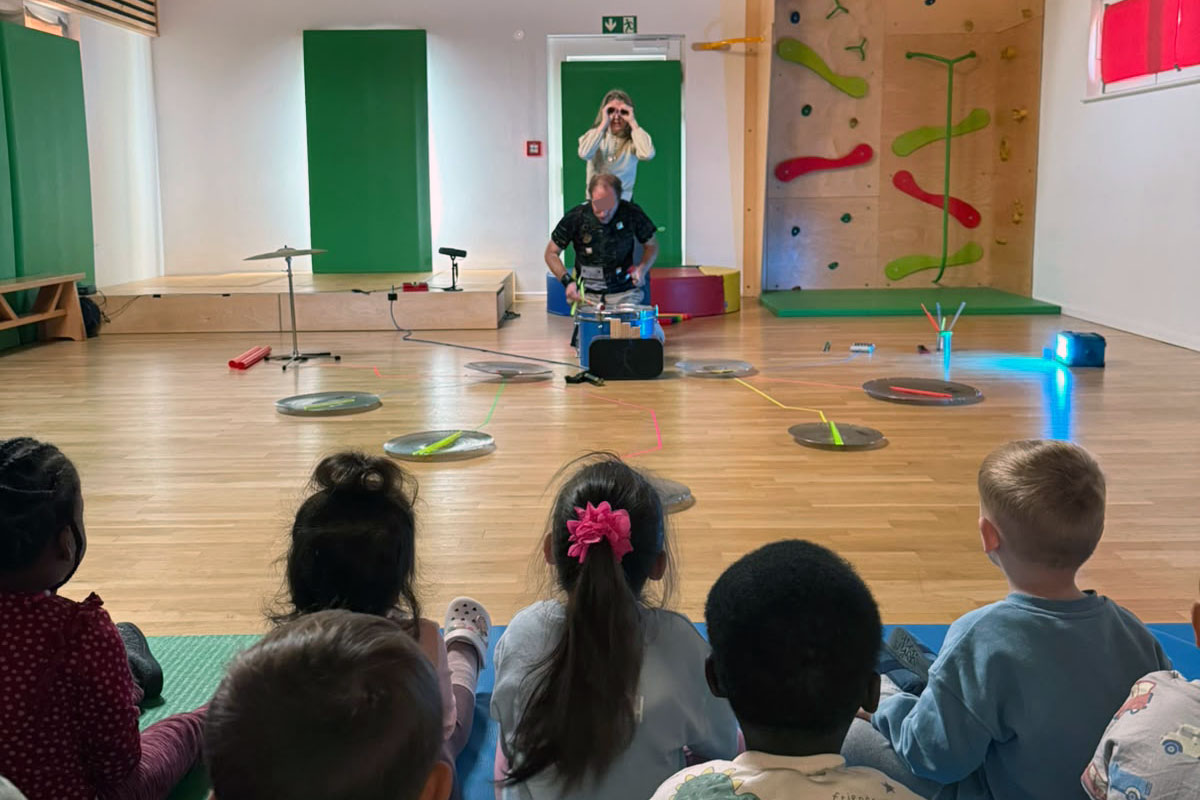 Kinder (von hinten) schauen im Turnraum der Kita einer Theateraufführung zu